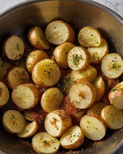 A baking sheet lined with parchment paper, with seasoned potato rounds arranged in a single layer. The image should show a hand placing the last slice to emphasize the neat, non-overlapping arrangement.