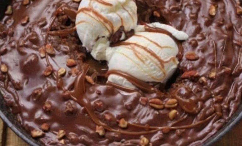 ustic-style dessert presented in a round, black cast iron skillet. The dessert is a rich, chocolate brownie topped with two scoops of vanilla ice cream.